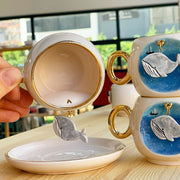 Ceramic coffee cup with whale artwork on blue panel, gold handle and interior.
