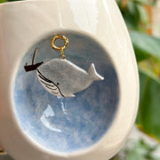 Blue whale mug close-up: gray whale graphic with gold loop on blue background
