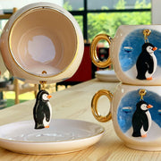 Ceramic coffee cup with penguin motif, gold handle and matching saucer