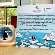 Ceramic coffee cup with penguin design and gold handle, on white saucer