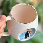 White ceramic mug with gold rim, penguin art on side, loop handle
