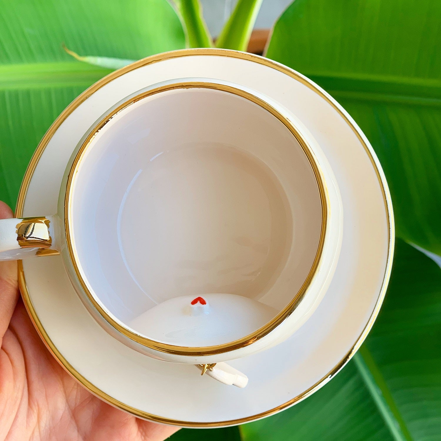 Top view of white tea cup with gold rim and handle, snowman charm hanging inside