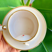 Top view of white tea cup with gold rim and handle, snowman charm hanging inside