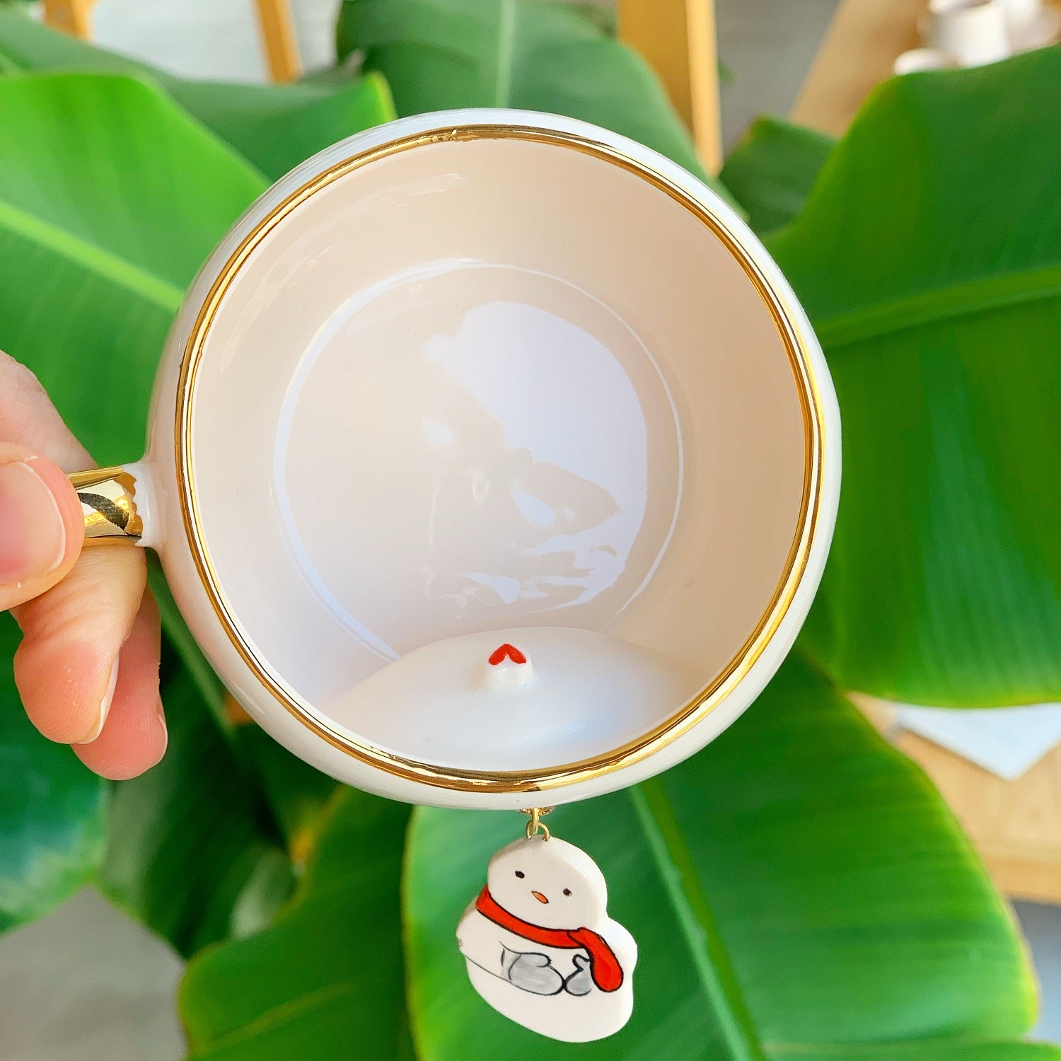 White tea cup with gold rim, snowman charm hanging inside near the handle