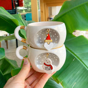 Two stacked white tea cups with gold rims, snowman charms hanging from each cup