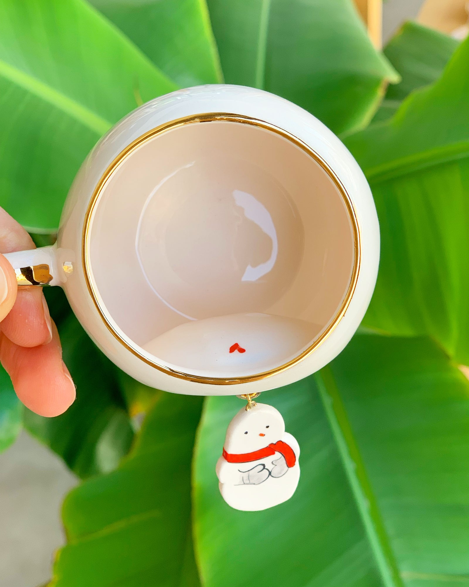 White coffee cup interior with gold rim and hanging snowman charm illustration.