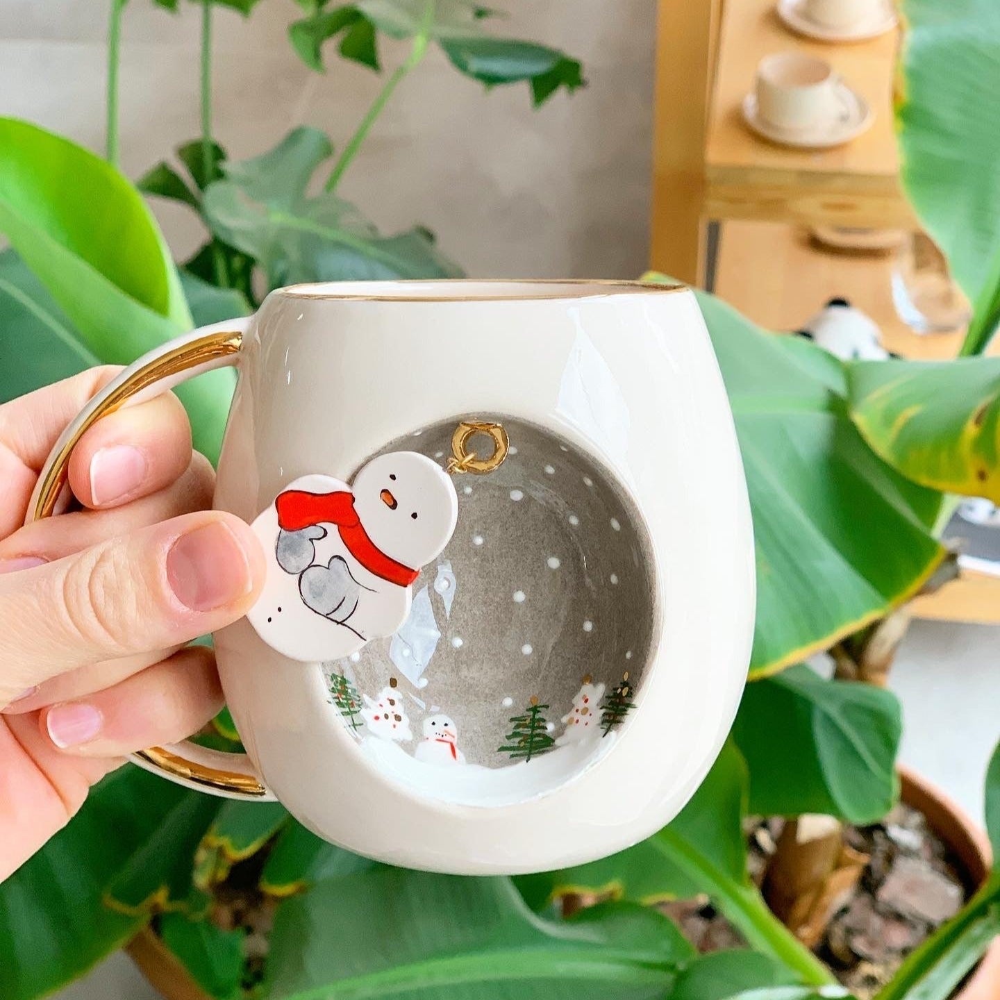 White ceramic mug with gold handle, snowman and small trees in oval winter graphic