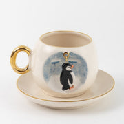 Ceramic coffee cup and saucer with penguin charm in blue splash print, gold handle