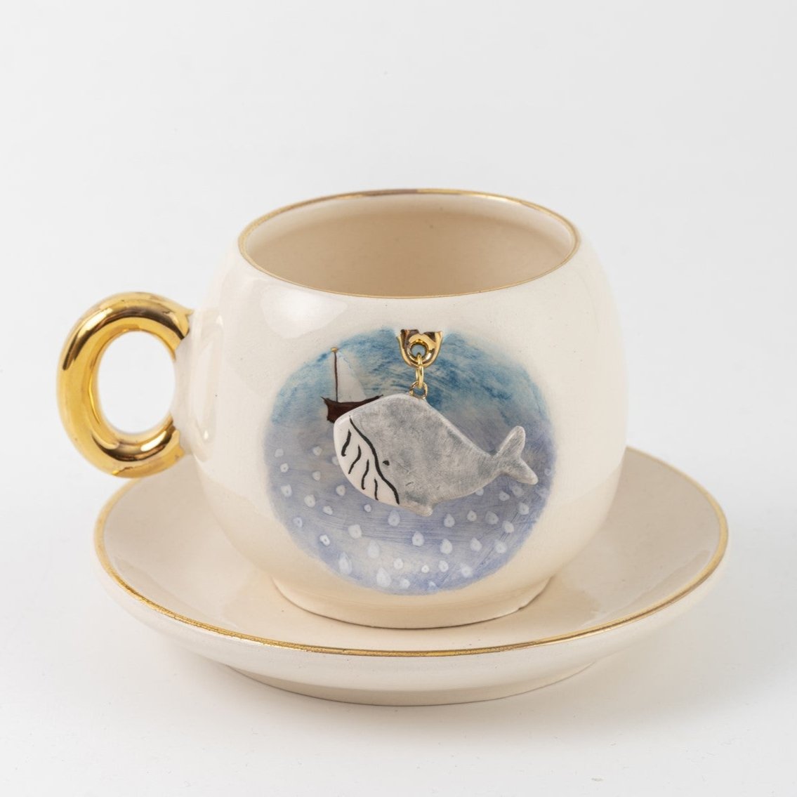 Ceramic coffee cup and saucer, blue whale design on front, gold handle and trim.