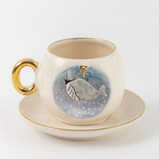 Ceramic coffee cup and saucer, blue whale design on front, gold handle and trim.