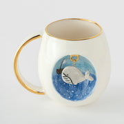 Porcelain mug with gold rim and handle, blue whale illustration on front