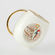 Porcelain mug with gold spout and handle, angled view, blue bird motif on white