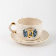Ceramic angel-wing letter mug with blue wings and gold D, on matching saucer
