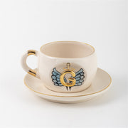 Ceramic angel-wing letter mug with blue wings and gold G, on matching saucer