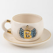 Ceramic angel-wing letter mug with blue wings and gold B, on matching saucer