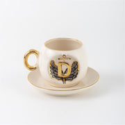 Porcelain cup and saucer with gold handle, black angel wing motif, letter D