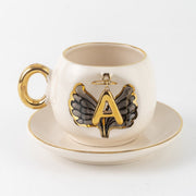 Porcelain cup and saucer with gold trim, black angel wing motif, letter A