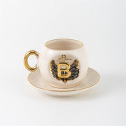 Porcelain cup and saucer with gold handle, black angel wing motif, letter B