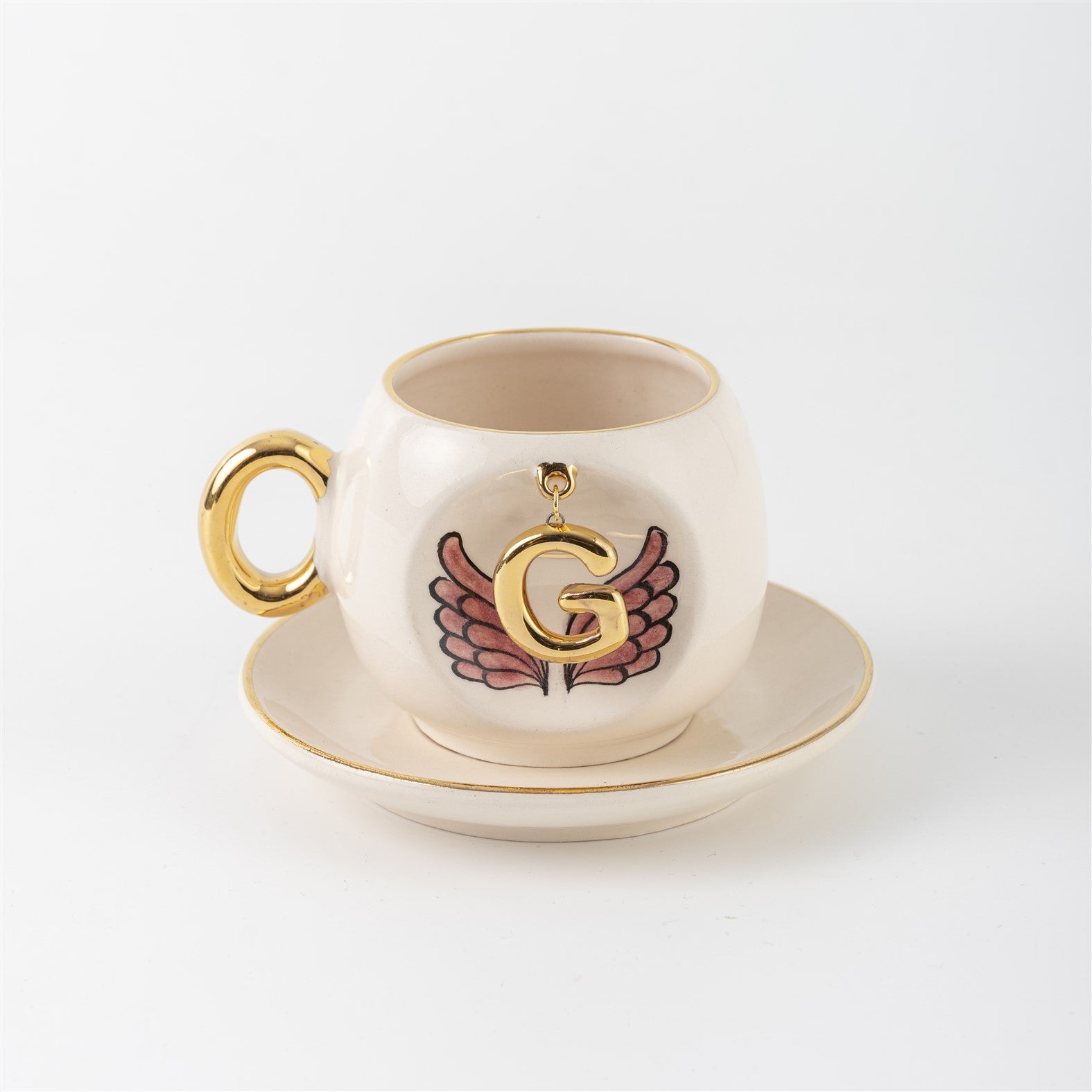 Ceramic coffee cup with gold handle, pink winged letter G charm and saucer.