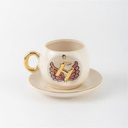 Ceramic coffee cup with gold handle, pink winged letter H charm and saucer.
