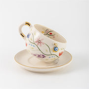 Tea cup and saucer set with floral painting, blue eye detail, and gold handle