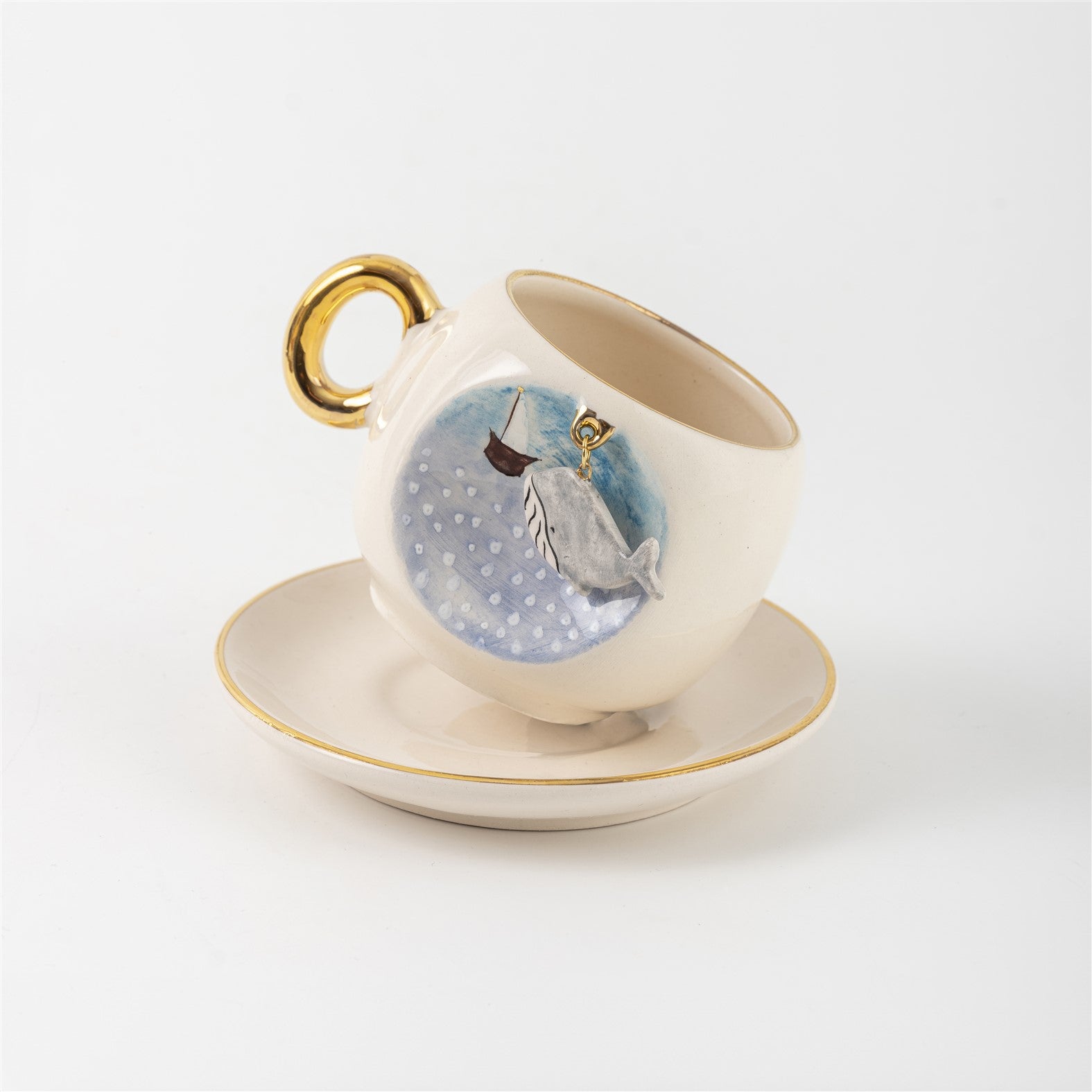 Ceramic coffee cup and saucer with blue whale scene on front, gold handle.