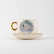 Ceramic coffee cup and saucer with blue whale illustration, gold handle, wide rim.