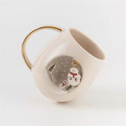 White ceramic mug with gold handle, snowman and pine trees visible on side panel