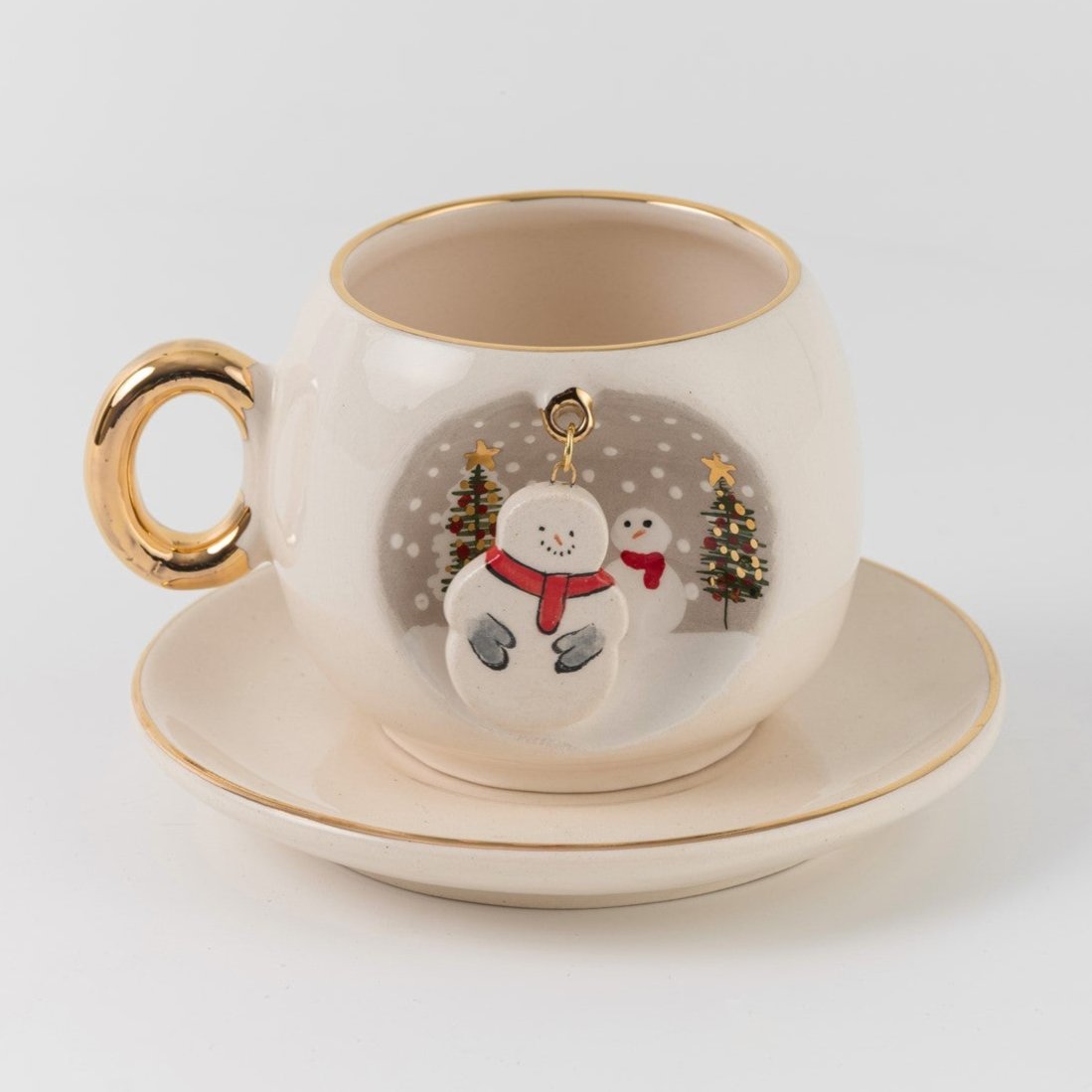 White ceramic snowman coffee cup and saucer set with gold handle, gold rim, winter scene badge.