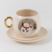 White ceramic snowman coffee cup and saucer set with gold handle, gold rim, winter scene badge.