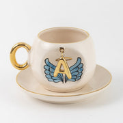 Ceramic coffee cup and saucer with gold A, blue angel wings, and curved gold handle