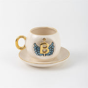Ceramic coffee cup and saucer with gold B, blue angel wings, and curved gold handle