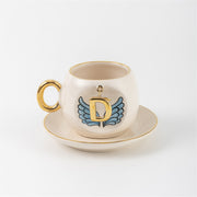 Ceramic coffee cup and saucer with gold D, blue angel wings, and curved gold handle