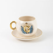 Ceramic coffee cup and saucer with gold G, blue angel wings, and curved gold handle