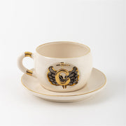 Porcelain mug on saucer with angel wing letter emblem and gold handle accents