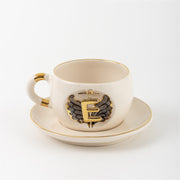 Porcelain mug and saucer with angel wing badge and gold letter E, cream base