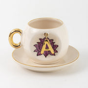 Ceramic coffee cup and saucer with gold handle, lotus letter A emblem on front