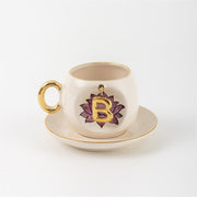 Ceramic coffee cup and saucer with gold handle, lotus letter B emblem on front