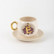 Ceramic coffee cup and saucer with gold handle, lotus letter E emblem on front