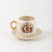 Ceramic coffee cup and saucer with gold handle, lotus letter G emblem on front