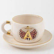 Porcelain mug and saucer set with gold rim, white body, and angel-wings letter print