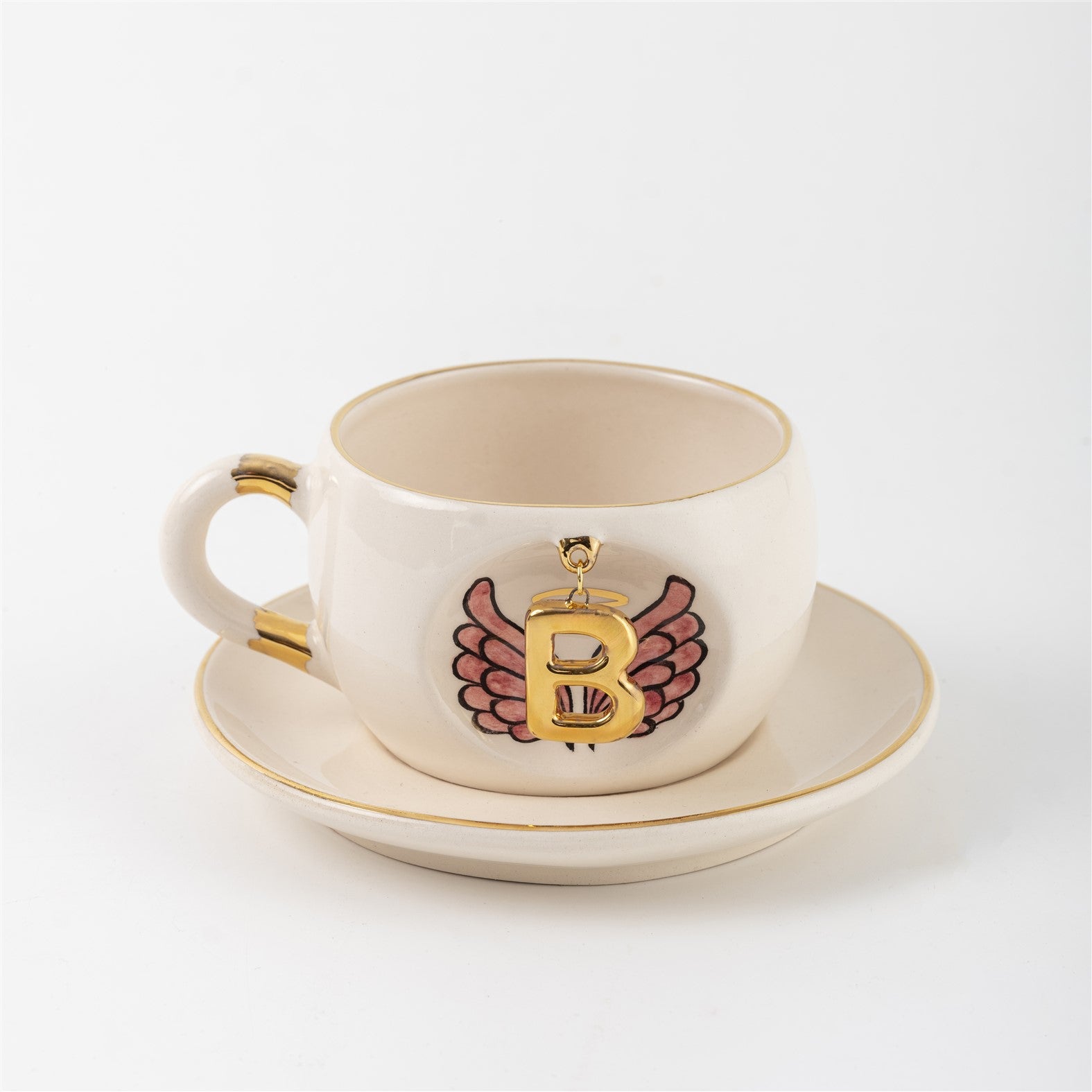 White porcelain mug with gold-accent handle and saucer, featuring angel-wings letter design