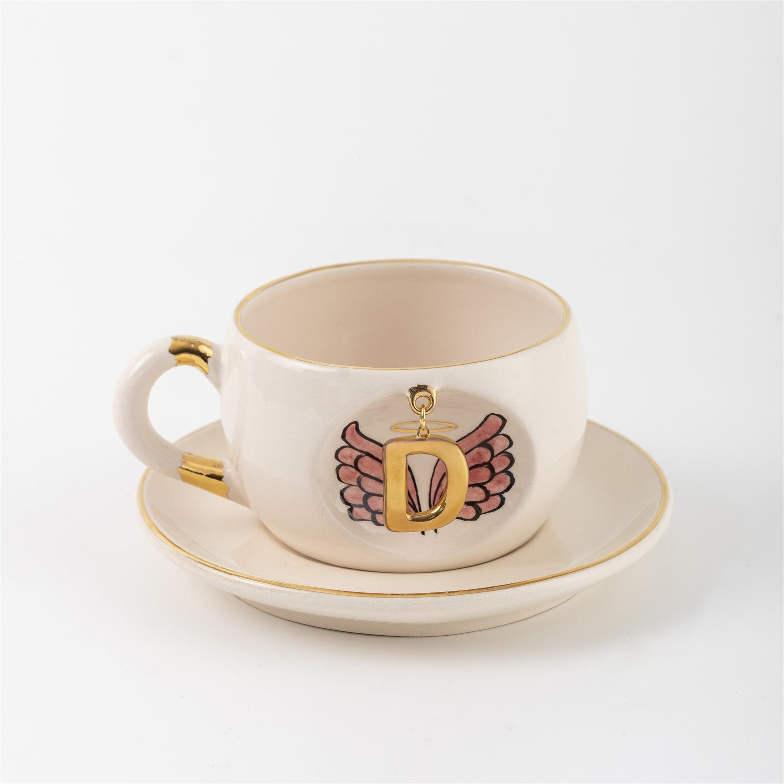 White ceramic mug with gold rim and handle accents, angel-wings letter artwork on front