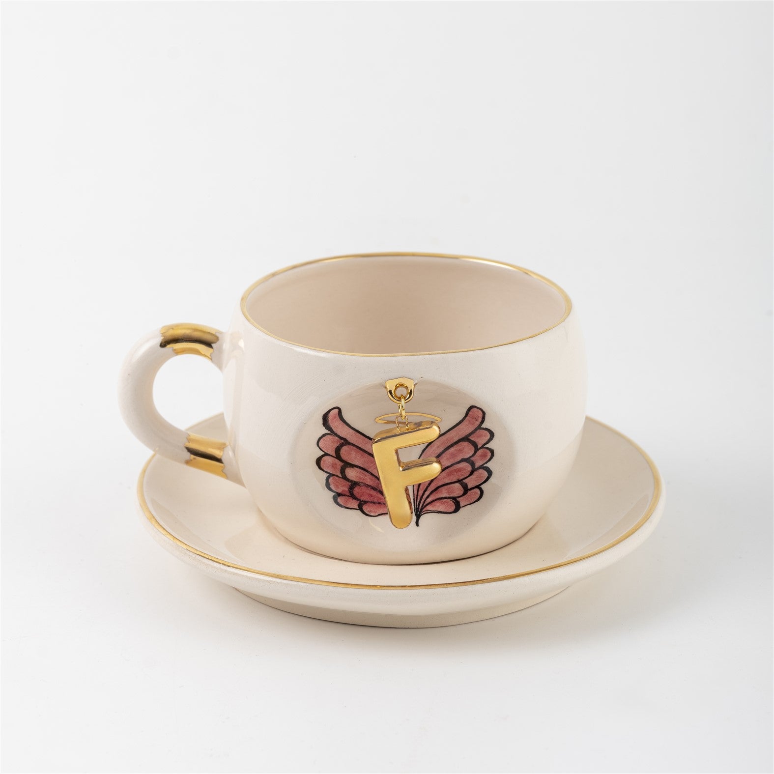 White mug with gold-rimmed opening and saucer, showing angel-wings letter print