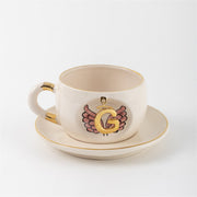 Porcelain cup and saucer set with gold trim, white finish, angel-wings letter emblem