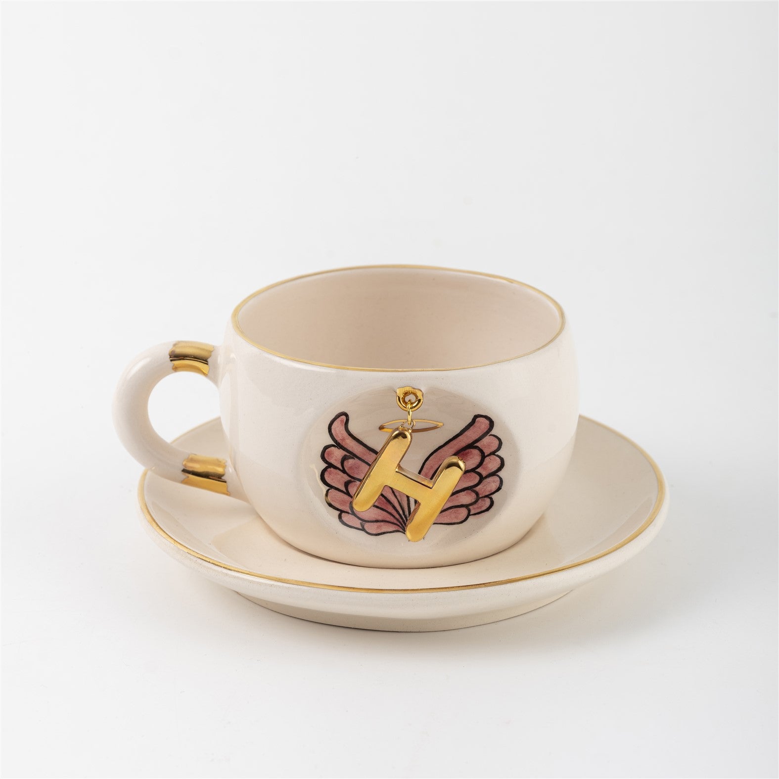 White ceramic mug with gold rim and handle accents, angel-wings letter print on side