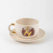 White ceramic mug with gold rim and handle accents, angel-wings letter print on side