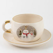 White tea cup and saucer with gold trim, snowman graphic and hanging charm