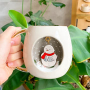 White ceramic mug with gold handle, centered snowman with red scarf and snowy dots