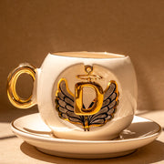 Porcelain tea cup and saucer set, white with gold handle and winged letter emblem
